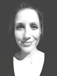 Close-up portrait of a smiling young woman over black background