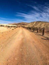 Dirt road amidst land against blue sky