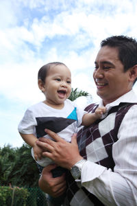 Father and baby boys against sky