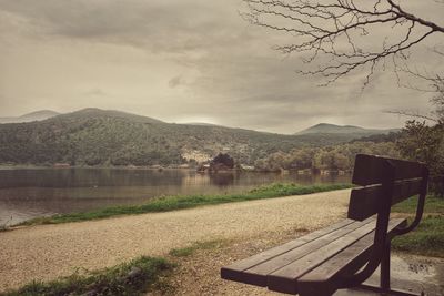 Empty bench by lake against sky