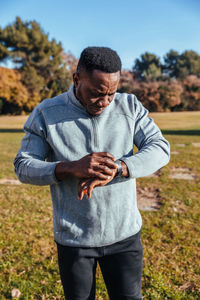 Young man in sportswear checking time while standing on field