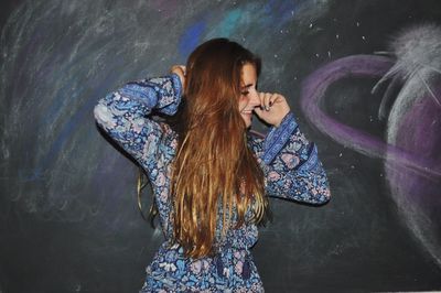 Rear view of woman standing against chalk drawing on blackboard