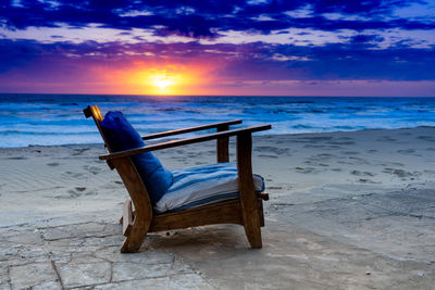 Chair on beach against sky during sunset