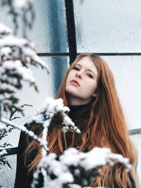 Portrait of young woman standing against window during winter