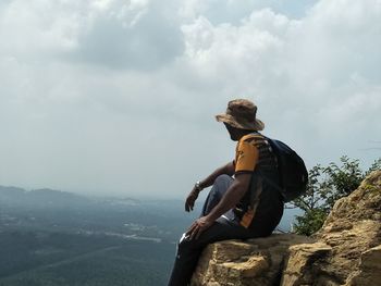 Man sitting on rock looking at mountain against sky
