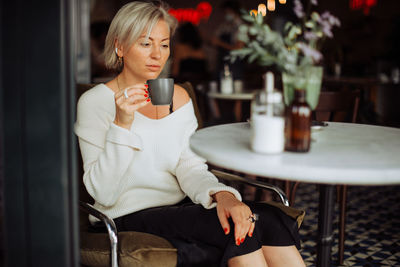 Woman drinking coffee looking sad while sitting alone at table in cafe