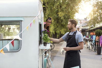 Female owner looking at male colleague arranging plants outside food truck on street