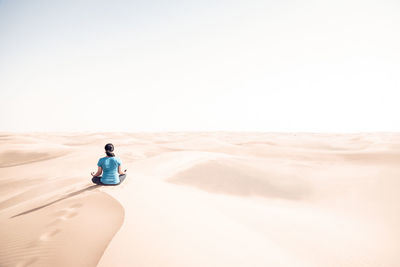Rear view of man sitting in desert against clear sky