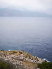 Rear view of woman standing on cliff in front of sea