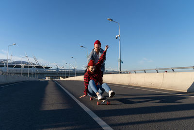 Outdoor leisure activity for lovers couple. hipster man push laughing woman sitting on longboard