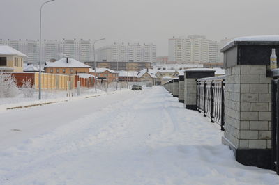 Snow covered houses by buildings in city against sky