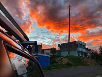 Road by buildings against sky during sunset