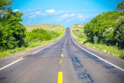 Empty road along trees and plants against sky