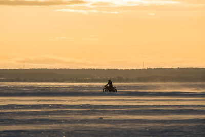 Silhouette person riding on frozen lake against sky during sunset