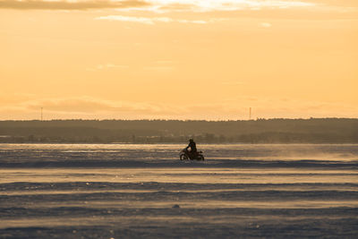 Silhouette person riding on sea against sky during sunset