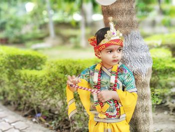 Cute baby in krishna costume standing against trees