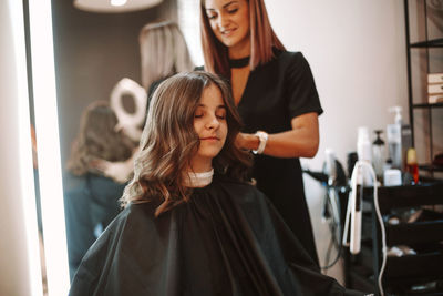 Smiling barber cutting hair of girl at salon