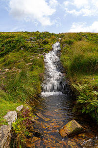 Scenic view of stream flowing through rocks against sky