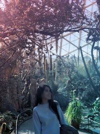 Smiling woman looking at trees and plants in greenhouse