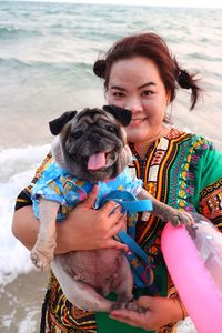 Portrait of woman holding pug at beach