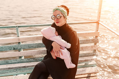 Portrait of woman carrying daughter while sitting against sea