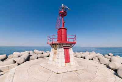 Lighthouse by sea against clear blue sky