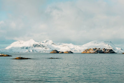 Scenic view of sea by snowcapped mountain against sky