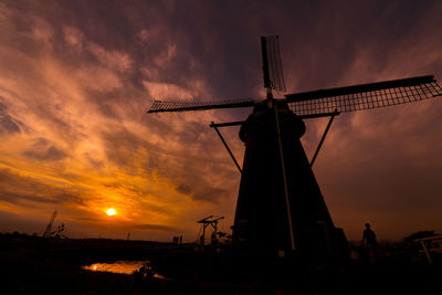 Silhouette traditional windmill against cloudy sky during sunset