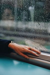 Cropped hand of woman on window sill during rainy season