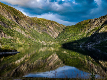 Scenic view of lake by mountains against cloudy sky