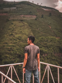 Rear view of man standing by railing against land