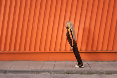 Cheerful african american woman in sportswear dancing in the street on an orange background