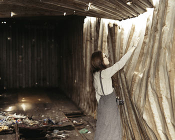 Side view of woman touching broken metal wall