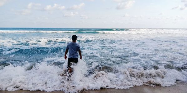 Rear view of man on sea shore against sky