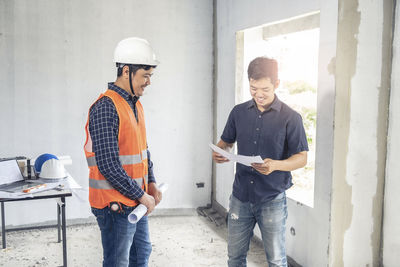 Smiling engineers holding blue prints at construction site