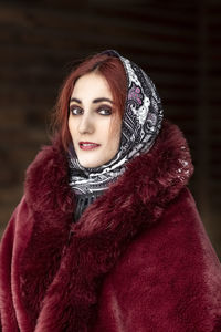 A slavic woman in a national colored scarf,a fur coat and  mittens on the porch of a wooden house