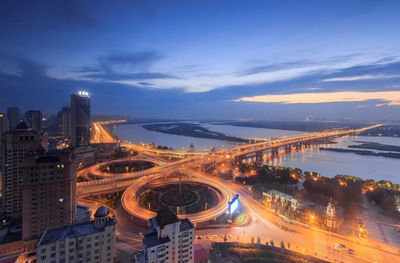 High angle view of illuminated street and buildings against cloudy sky at dusk