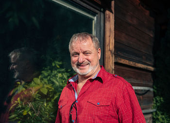 Cheerful bearded man in vibrant red shirt by his rustic cabin