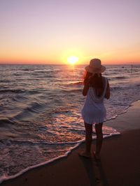 Rear view of woman standing on beach during sunset