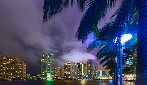 Illuminated modern buildings in city against sky at night