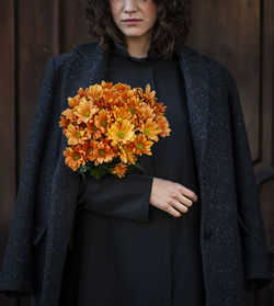 Midsection of woman holding flower bouquet standing by door