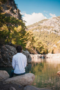 Rear view of man sitting on rock by lake