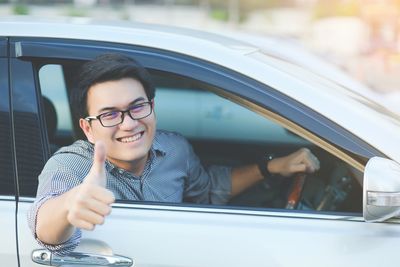 Portrait of smiling man gesturing thumbs up while sitting in car