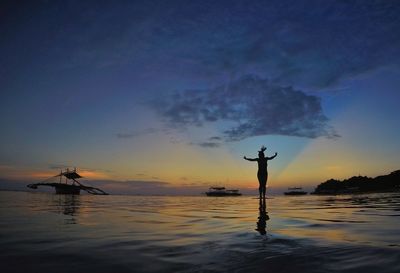 Silhouette person standing in sea against sky during sunset