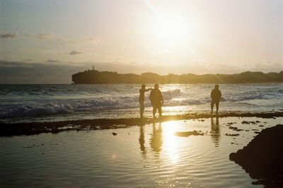 Silhouette people on beach against sky during sunset