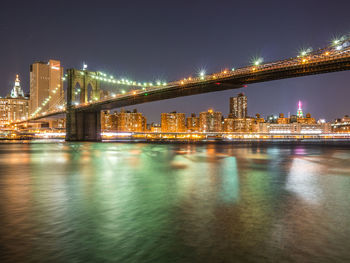 Illuminated bridge over river with city in background