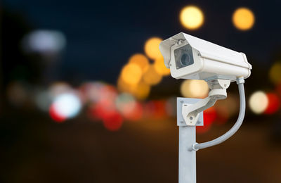 Close-up of security camera against illuminated lights at night