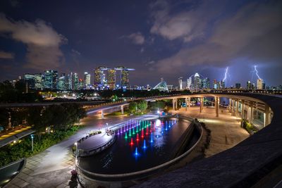 Illuminated bridge by buildings against sky at night