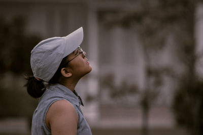 Close-up of teenager girl in casual clothing with hat standing and looking up 