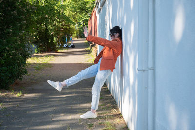 A young brunette girl in an orange jacket takes a selfie against a brick wall